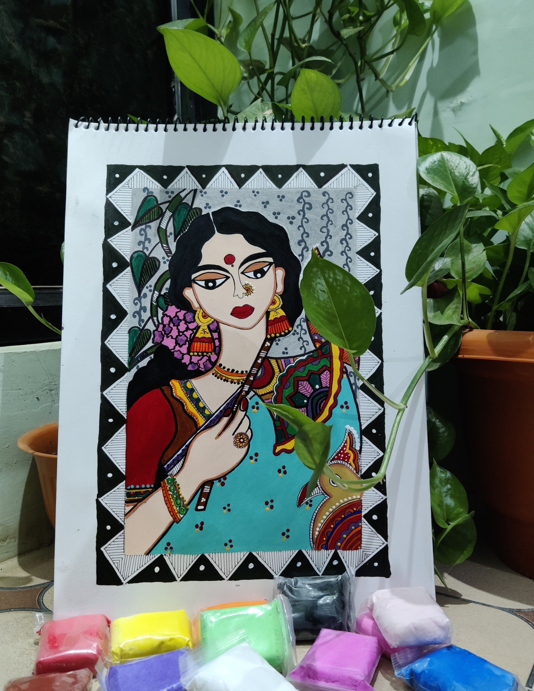 Portrait of a woman with patterned shawl, presented with a row of Holi color packets.