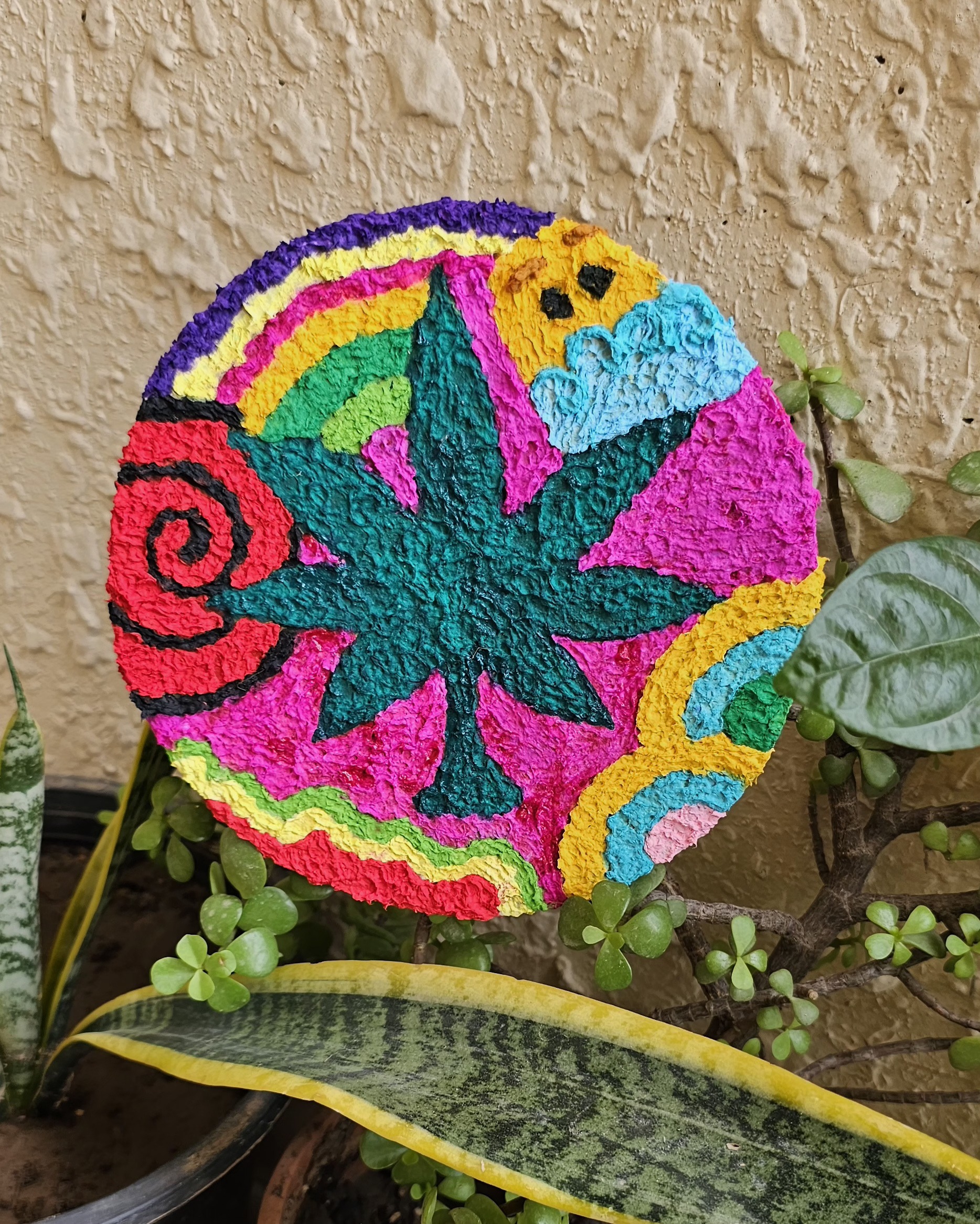 Circular relief with a stylized leaf radiating from sun and moon, in raised tissue texture.
